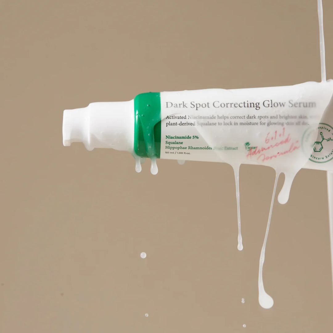 Tube of Dark Spot Correcting Glow Serum with white cream spilling out on a beige background