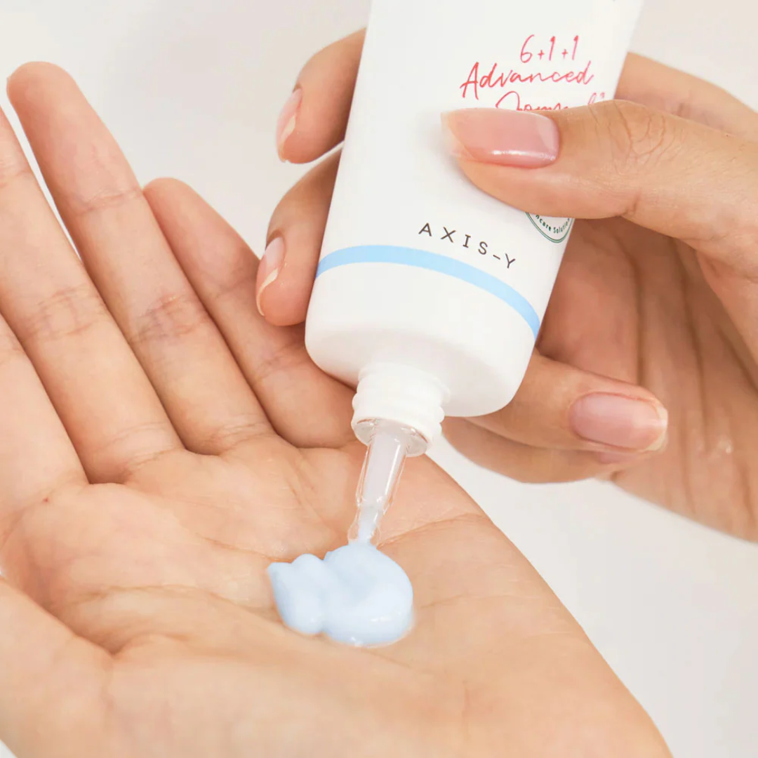 Hand holding a tube of AXIS-Y skincare product with cream being applied to the palm.