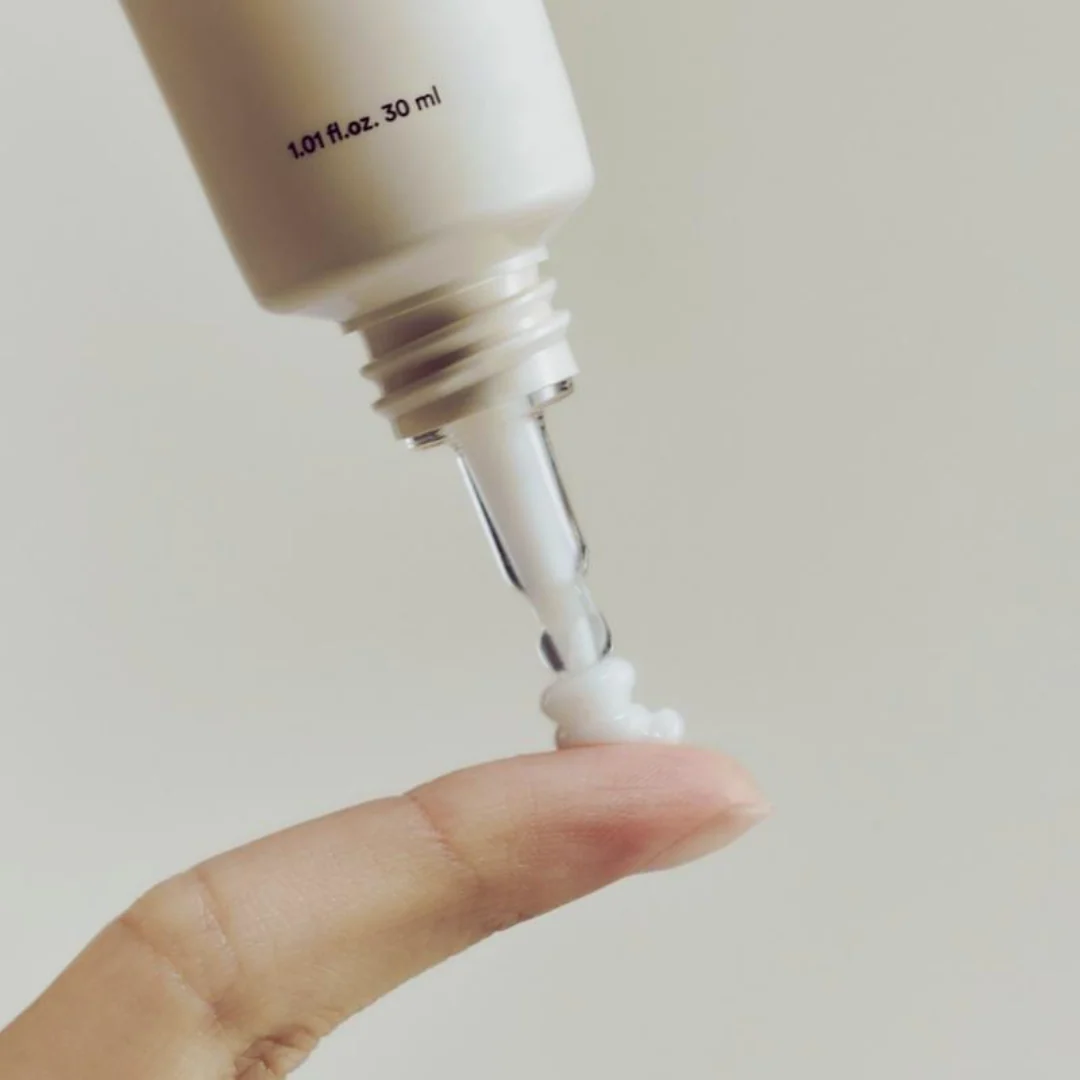 Close-up of a dropper bottle with liquid being dispensed onto a finger against a plain background