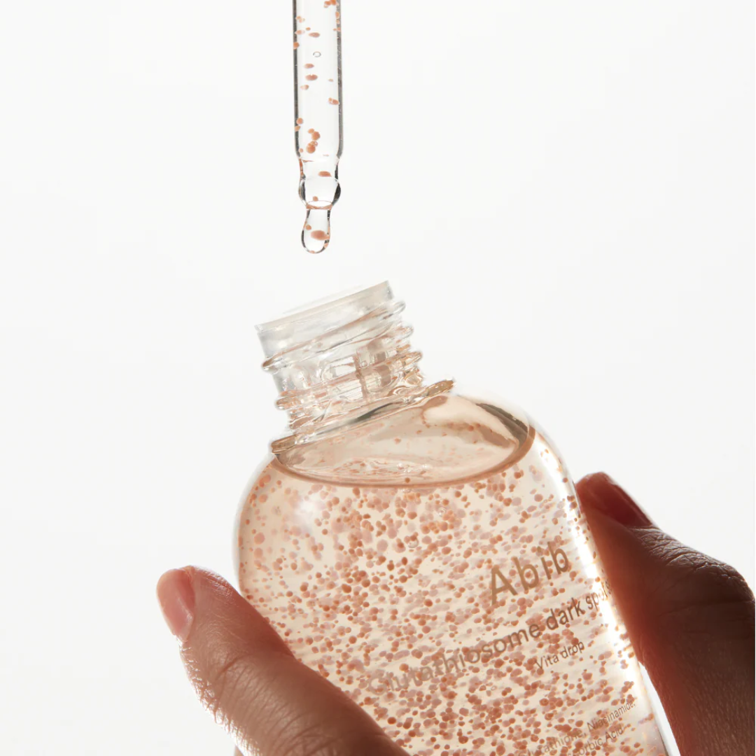 Hand holding a clear bottle with a dropper, filled with a pinkish liquid, on a white background.