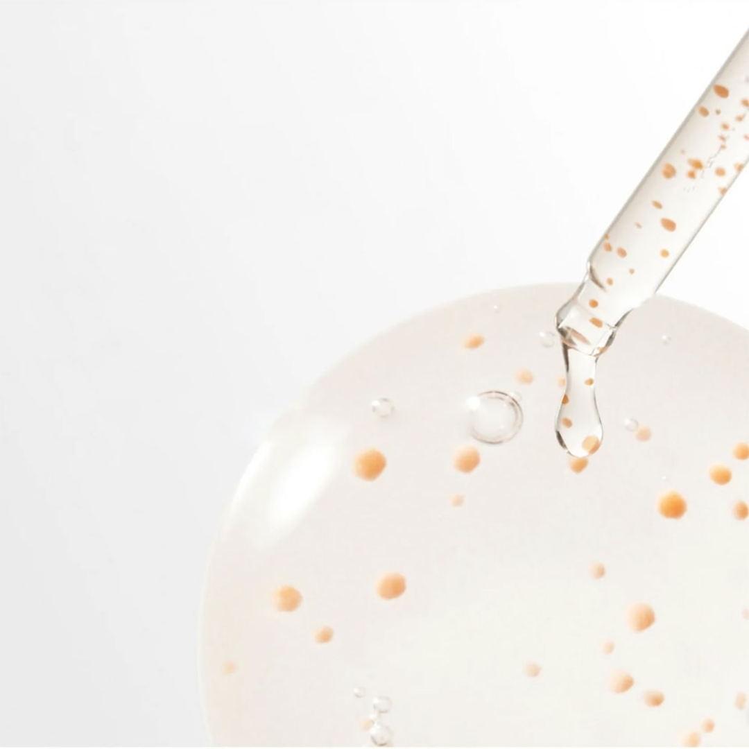 Close-up of a dropper with liquid being applied to a white surface with orange specks.