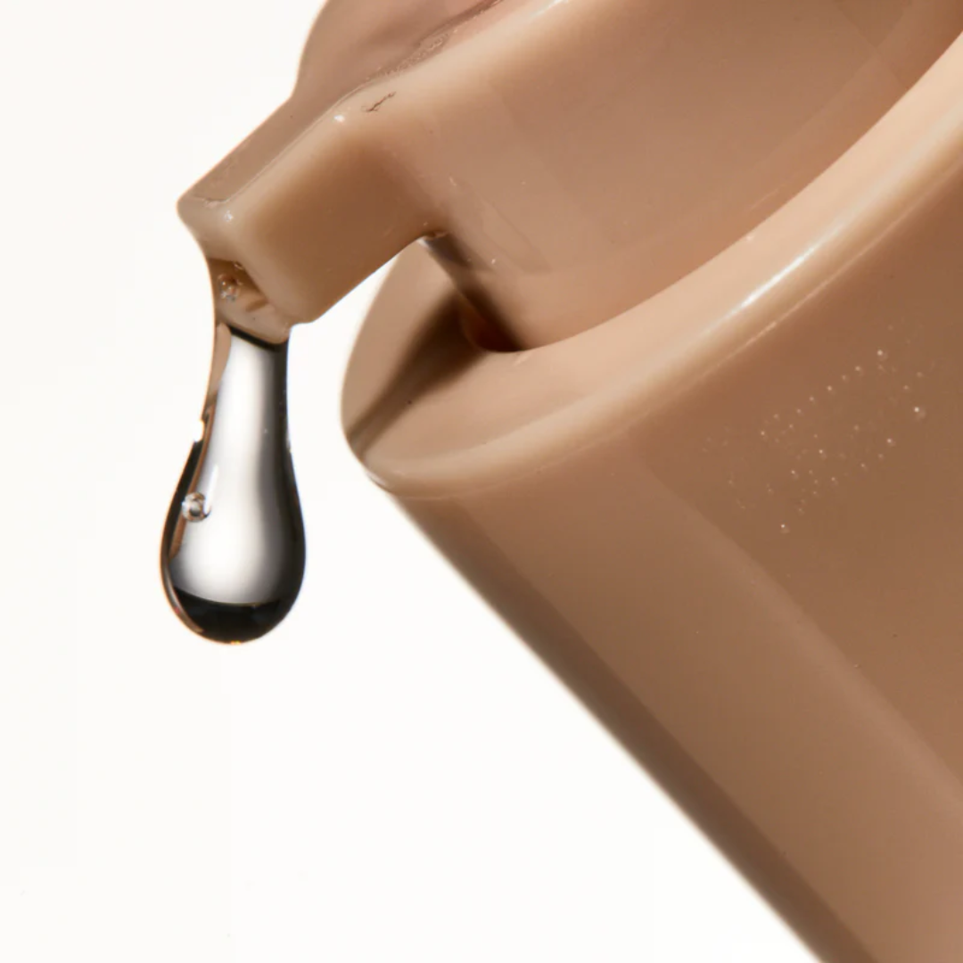 Close-up of a beige ceramic pitcher with a droplet of liquid on a white background