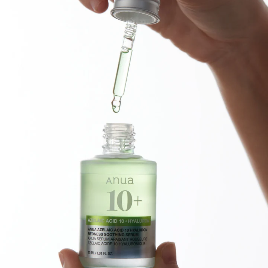 Hand holding a dropper over a bottle labeled 'Anua 10+' on a white background
