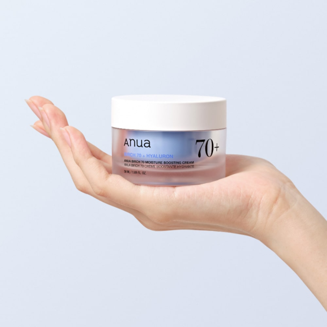 Hand holding a jar of Anua 70+ skincare cream against a light blue background
