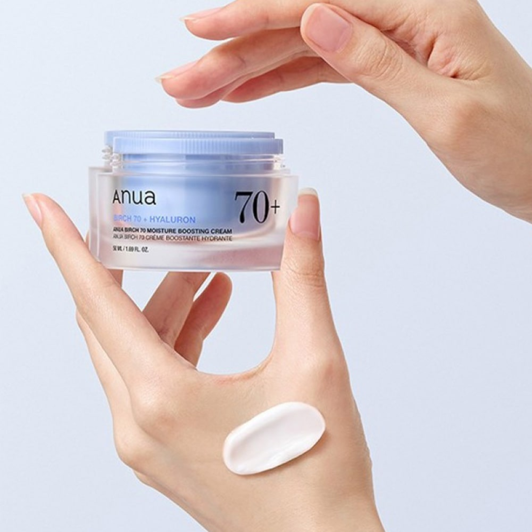 Hand holding a jar of Anua 70+ cream with a small amount on the palm against a light blue background