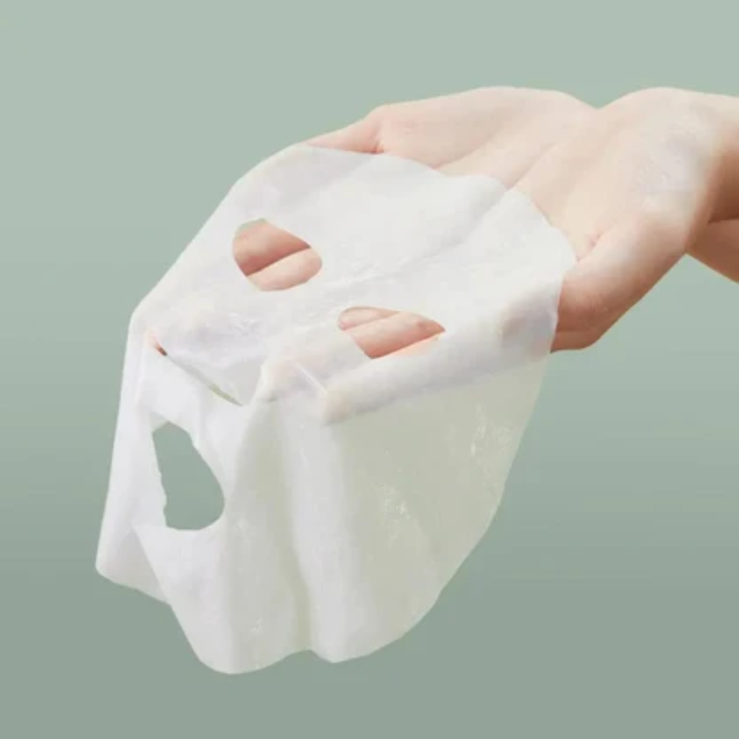 Hand holding a white mask against a light green background
