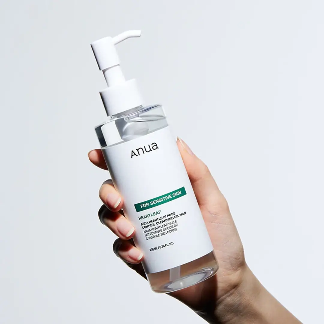 Hand holding a skincare bottle labeled 'Anua' against a light gray background