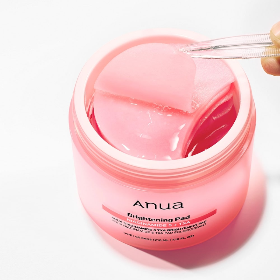Pink jar of Anua Brightening Pad with a hand holding a pad above it on a white background