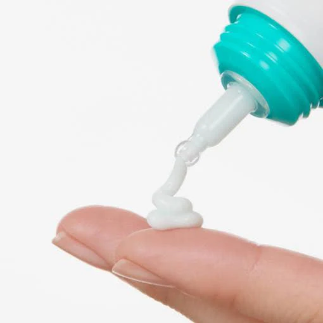 Green and white tube dispensing a white substance onto a person's palm against a white background