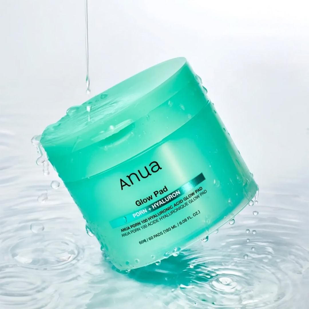 Green jar of Anua Glow Pad with water droplets on a light gray background