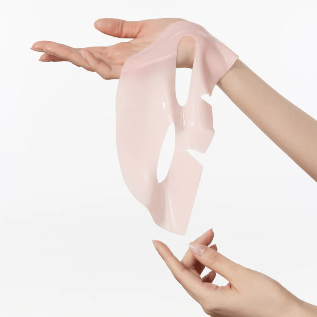 Hand holding a pink peach mask on a white background
