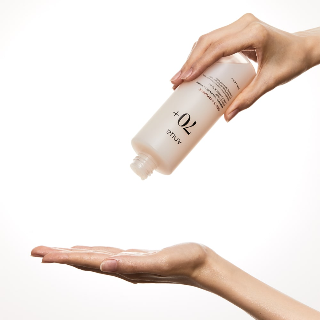 Hand holding a bottle of skincare product with another hand showing cream on palm against a white background