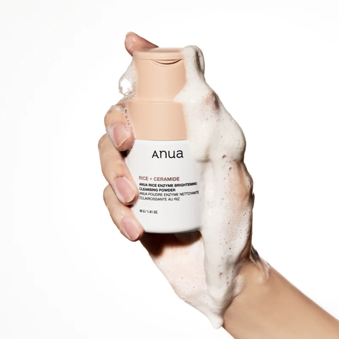 Hand holding a bottle of Anua skincare product with foam on a white background