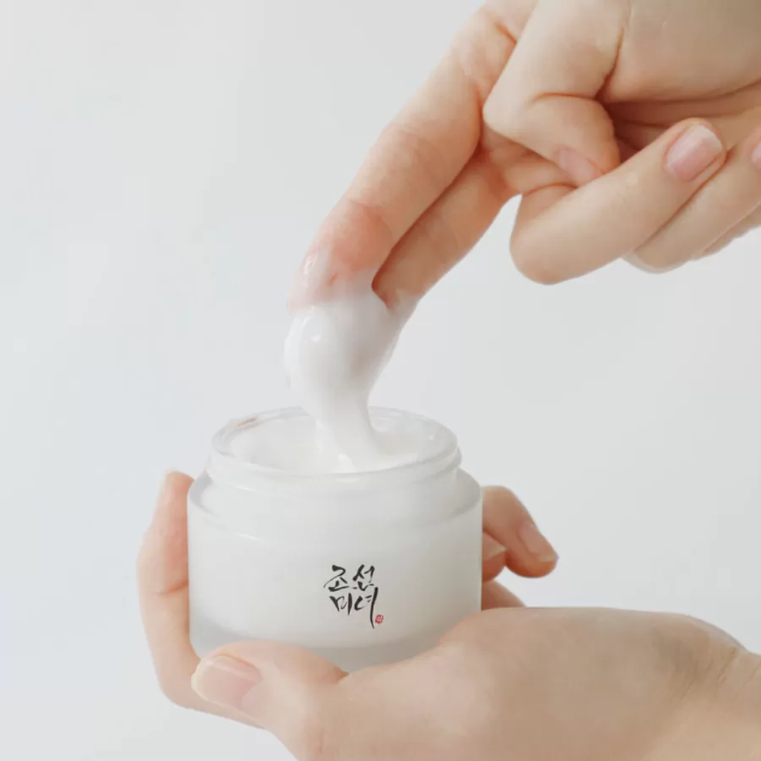 Hand applying cream from a jar with a white background