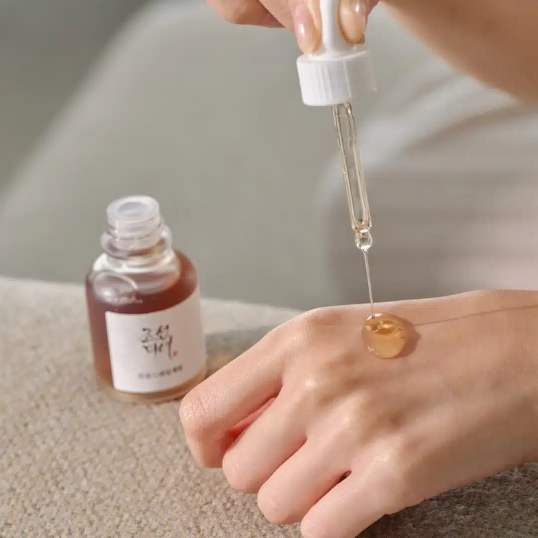 Person applying a dropper of liquid to their skin next to a bottle 