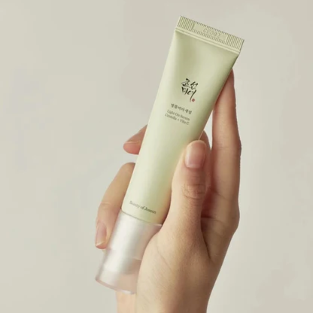 Hand holding a tube of skincare product against a plain background