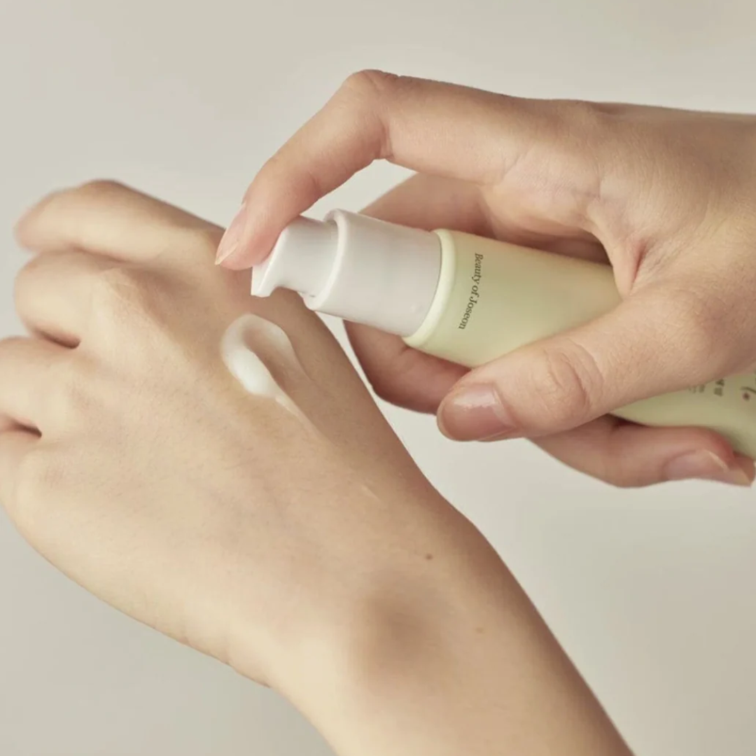 Hand applying a skincare product to another hand against a neutral background