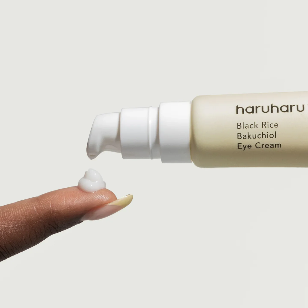 Haruharu Black Rice Bakuchiol Eye Cream with a hand applying cream on a light background