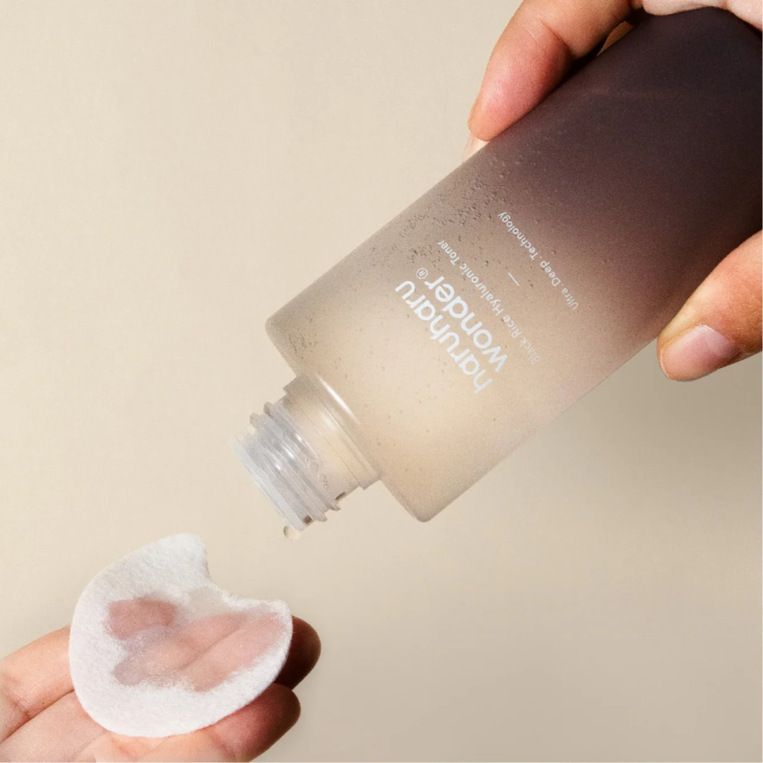 Person applying a skincare product from a bottle onto a cotton pad against a neutral background