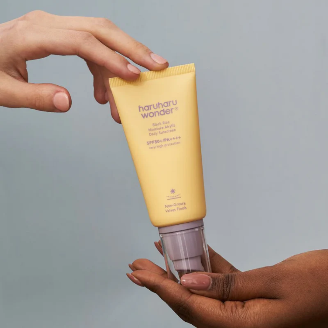 Two hands holding a yellow tube of haruhu wonder sunscreen against a gray background