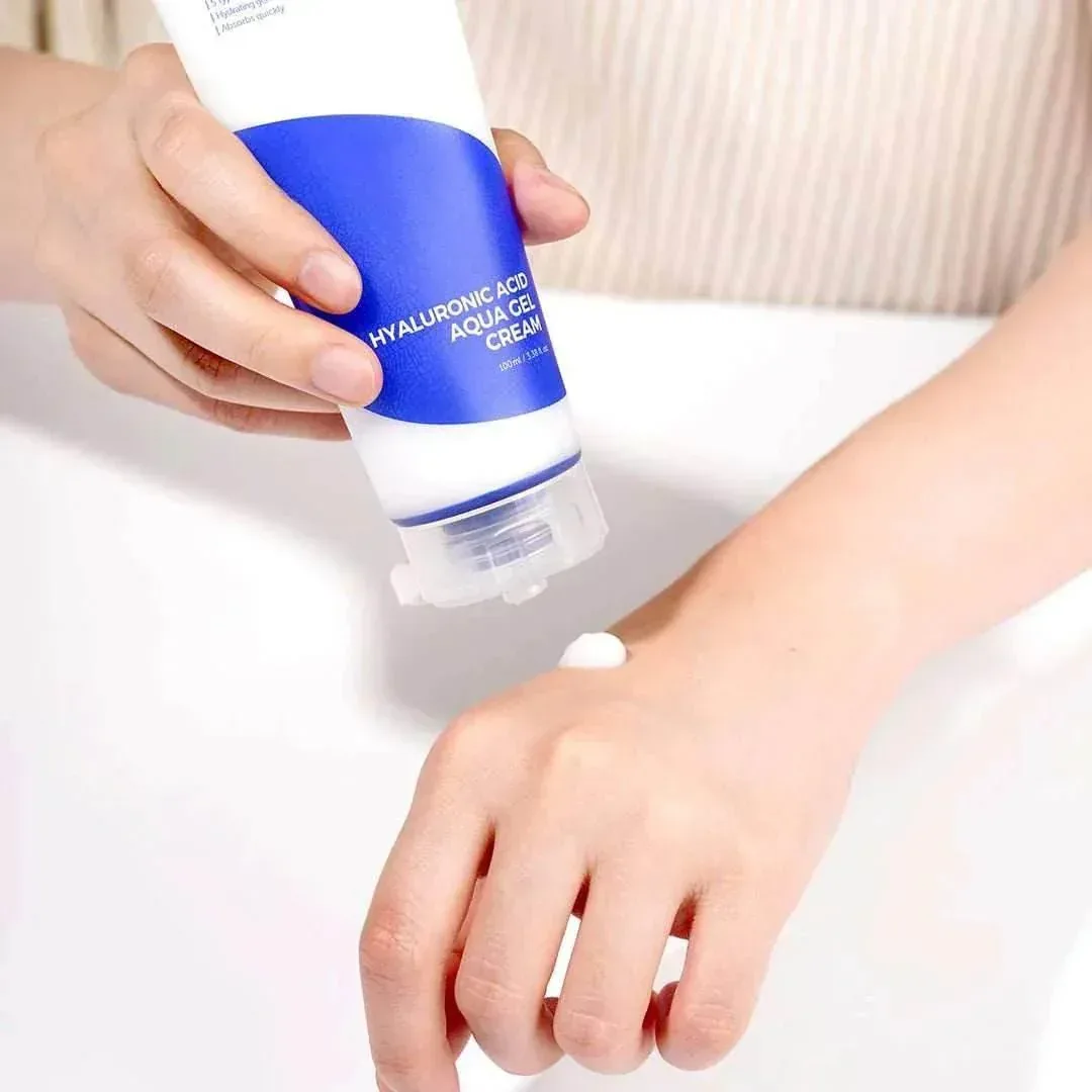 Person applying cream from a blue and white container labeled 'Hyaluronic Acid Aqua Cream' to their hand.