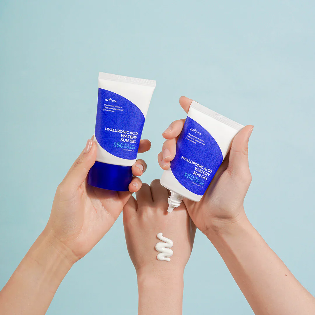 Two hands holding blue and white sunscreen bottles with a light blue background