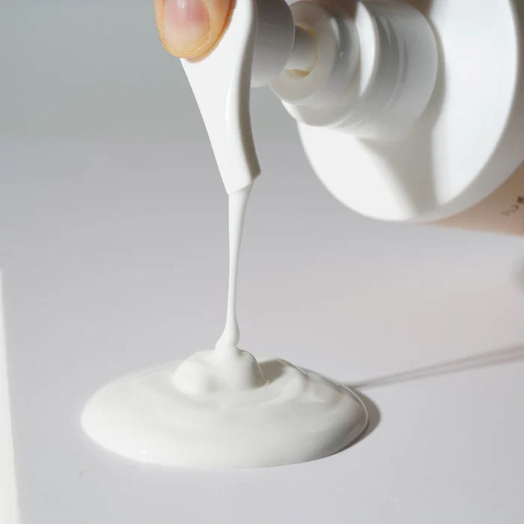 White cream being squeezed from a pump bottle onto a white surface.