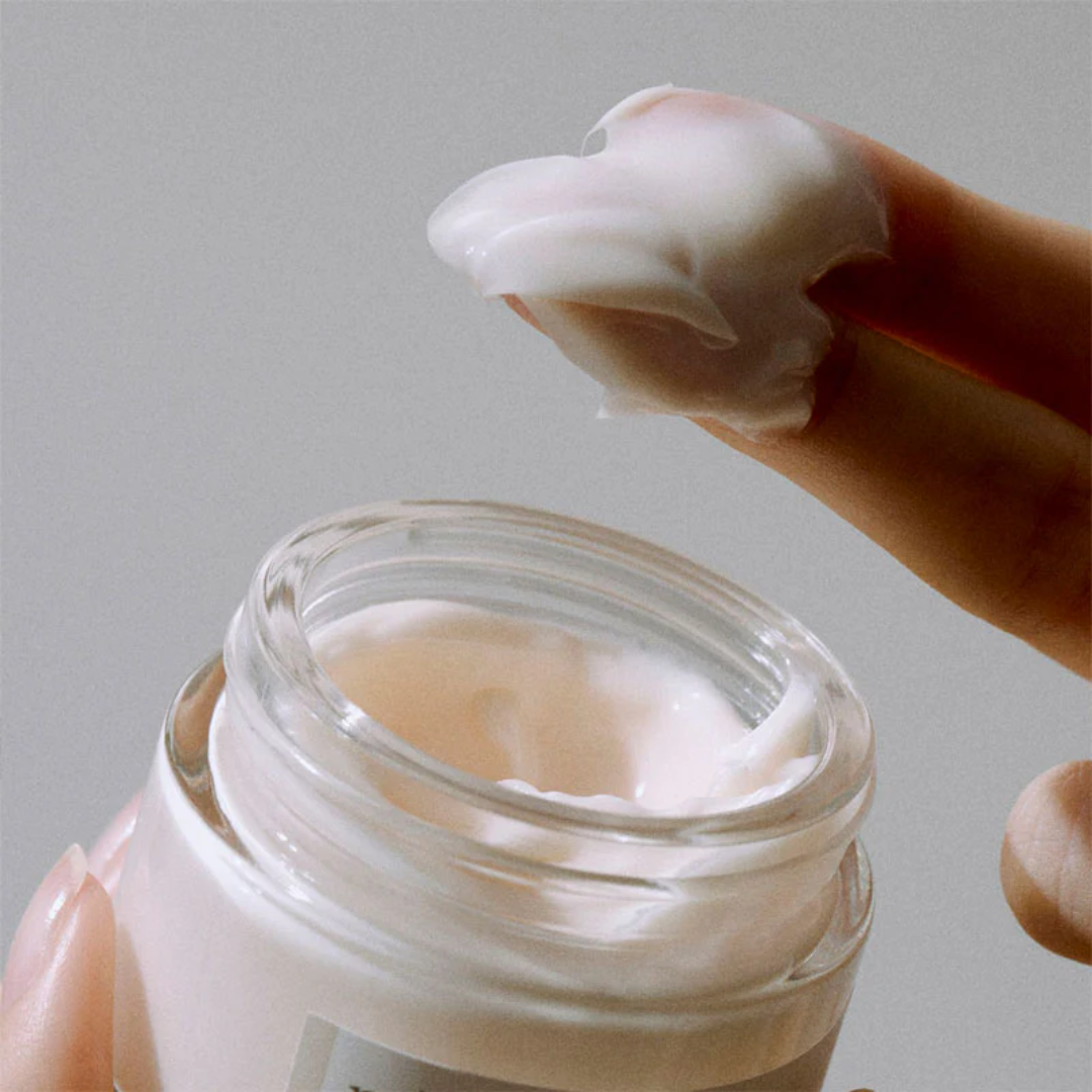 Hand applying cream from a jar with a neutral background