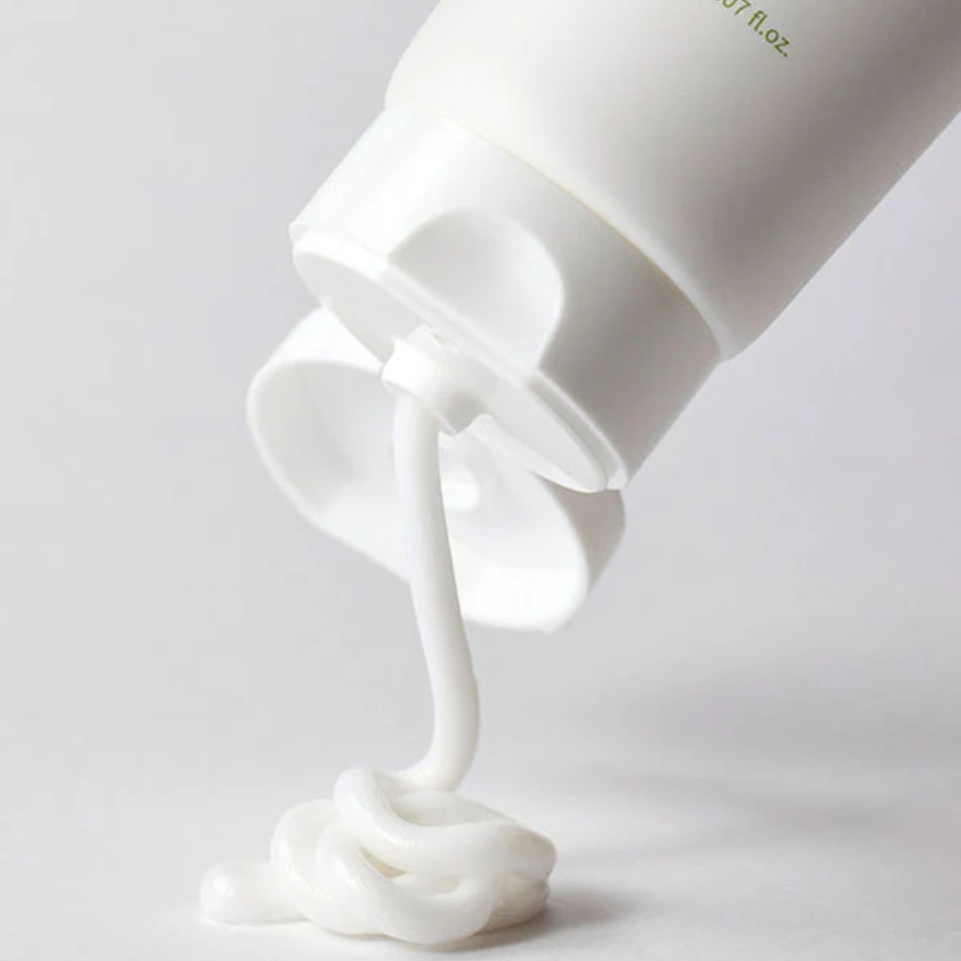 White cream being squeezed out of a container on a light gray background