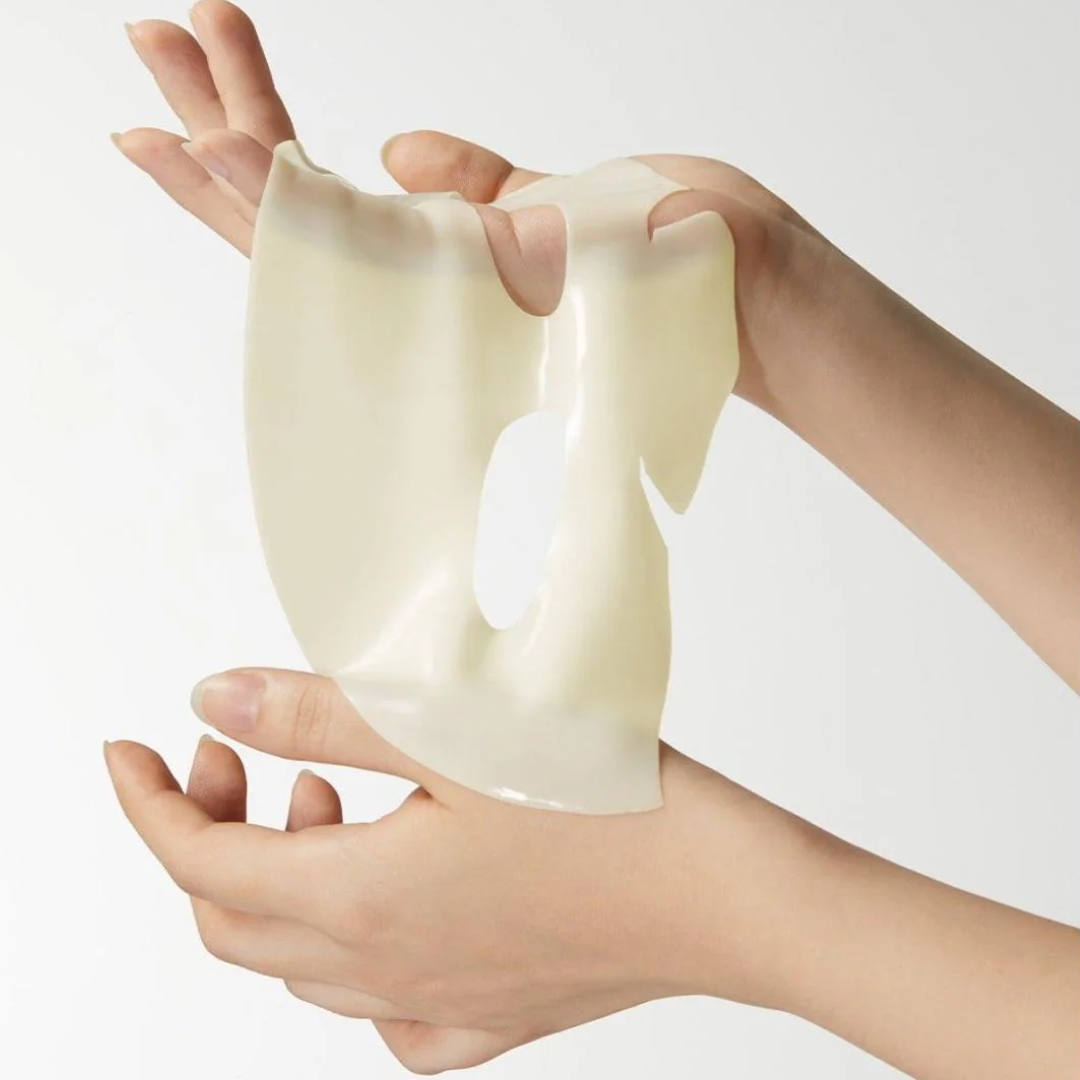 Hands holding a translucent, white mask against a plain background
