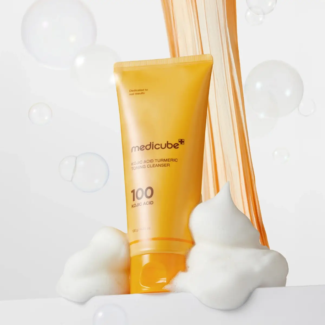 Orange tube of Medicube cleanser with white foam on a light gray background