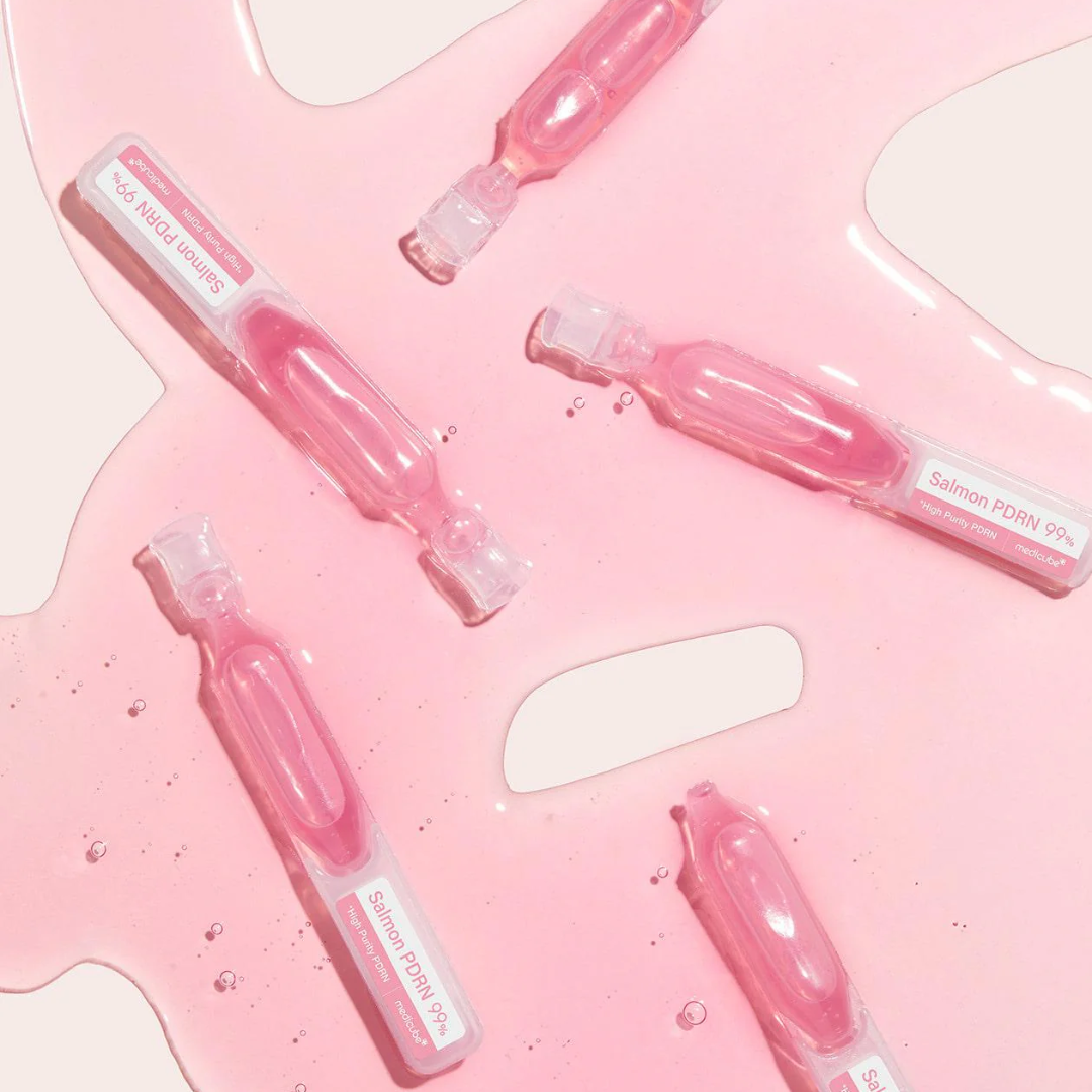 Pink skincare serum bottles with a mirror on a pink background