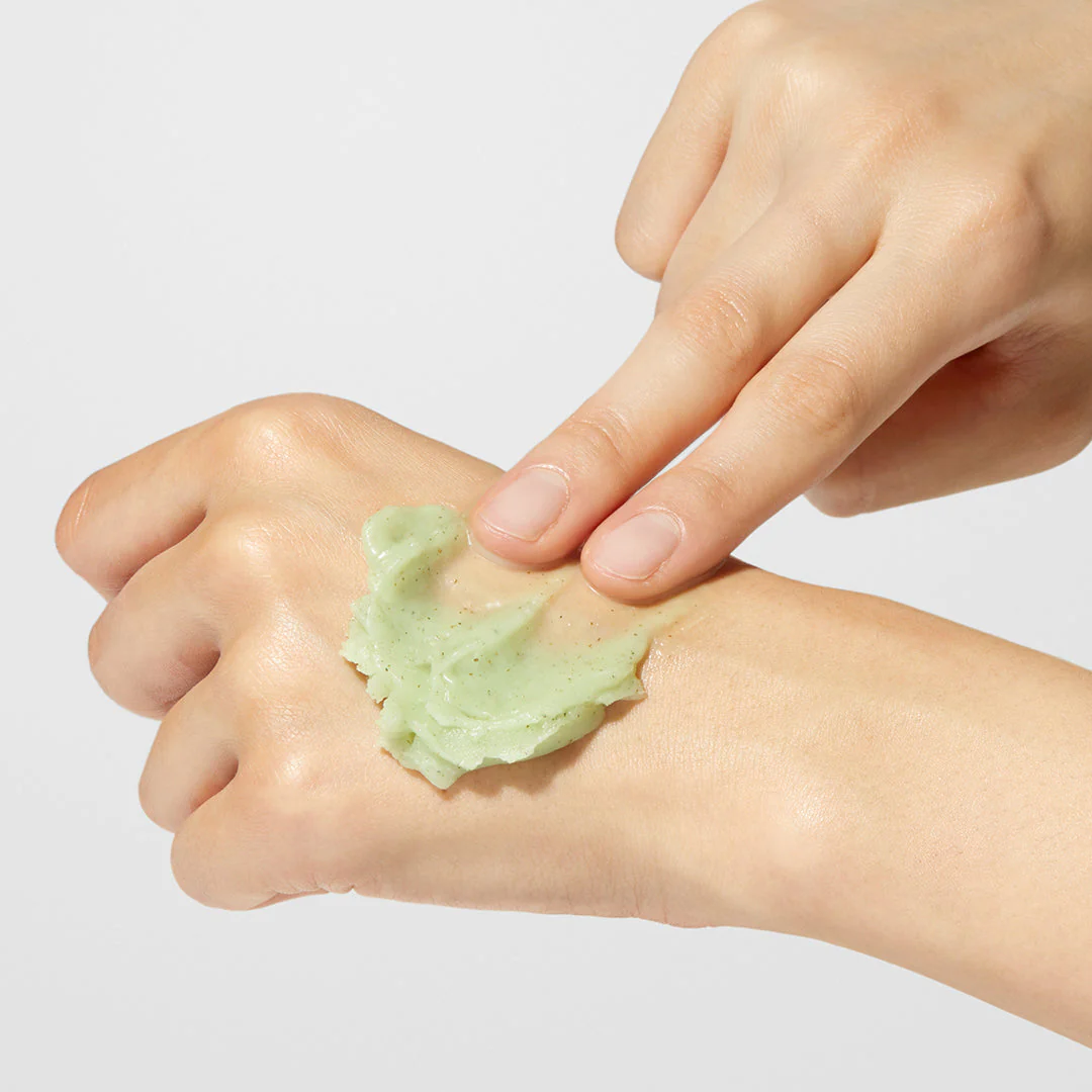 Hand applying green cream to another hand on a light gray background