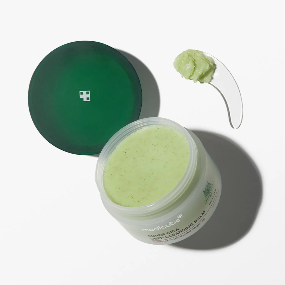 Open jar of green balm with a green lid and applicator on a white background