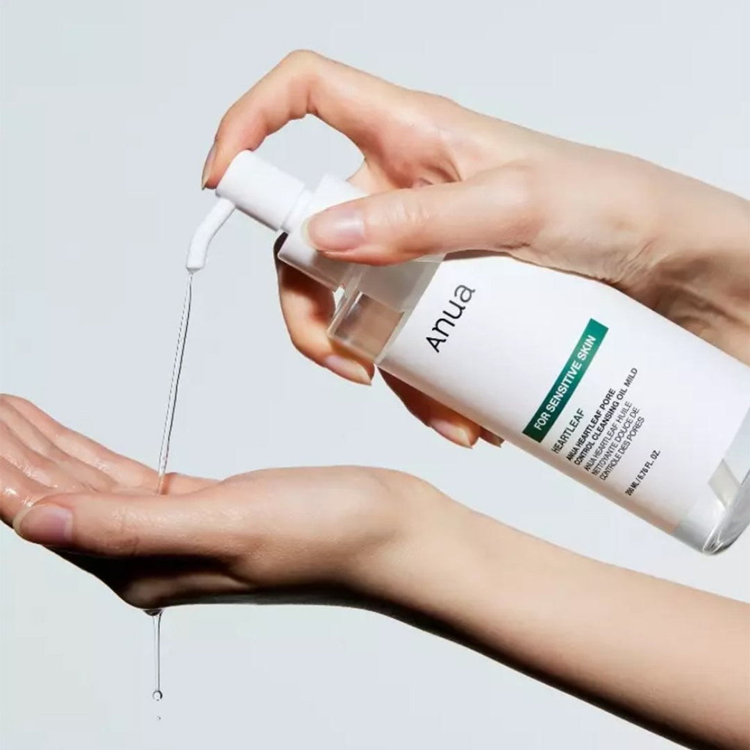 Hand holding a skincare bottle labeled 'ANUA' with dropper over another hand on a light background