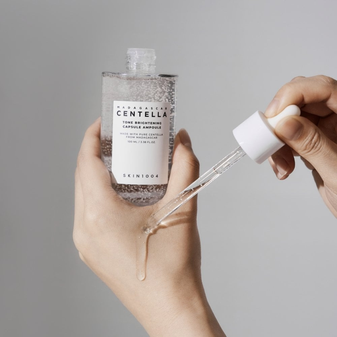 Hand holding a skincare bottle with a dropper against a gray background