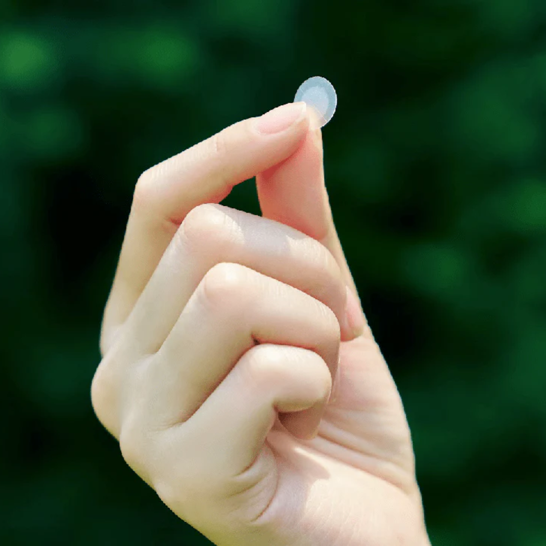 Hand holding a small clear object against a blurred green background