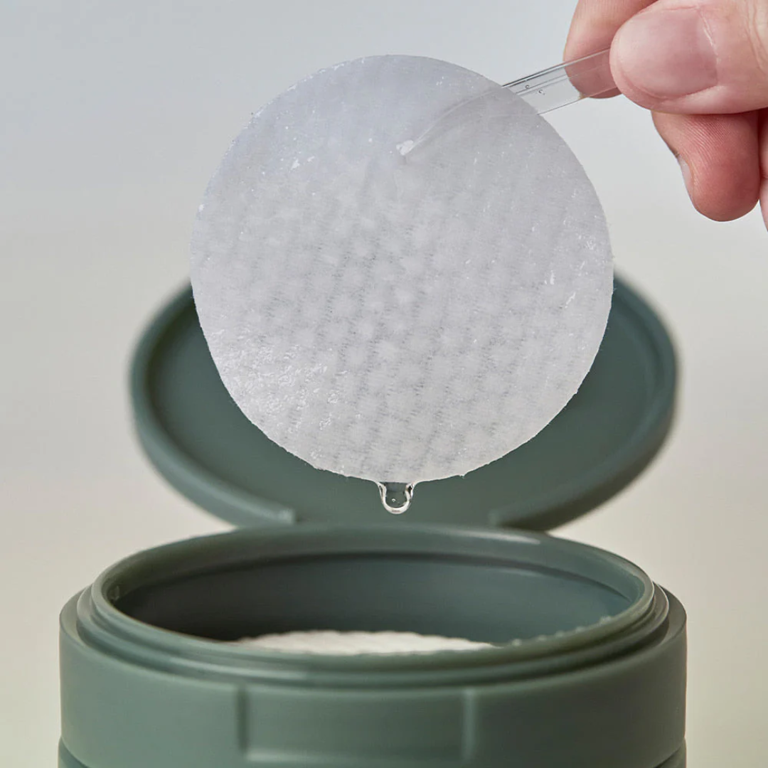 Hand using a tweezer to scoop out a white powder from a green container.
