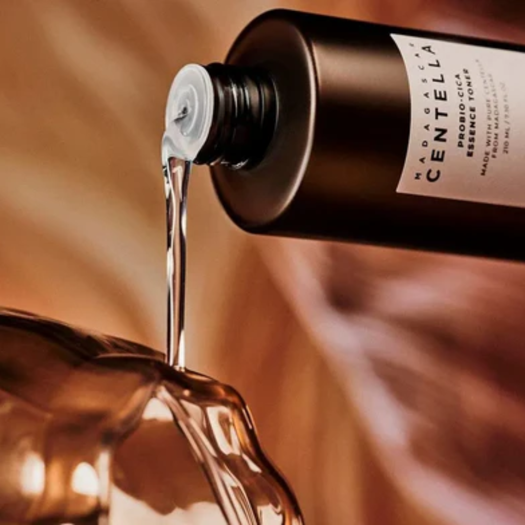 Bottle of Madarocella skincare product being poured into a glass container with a warm brown background.