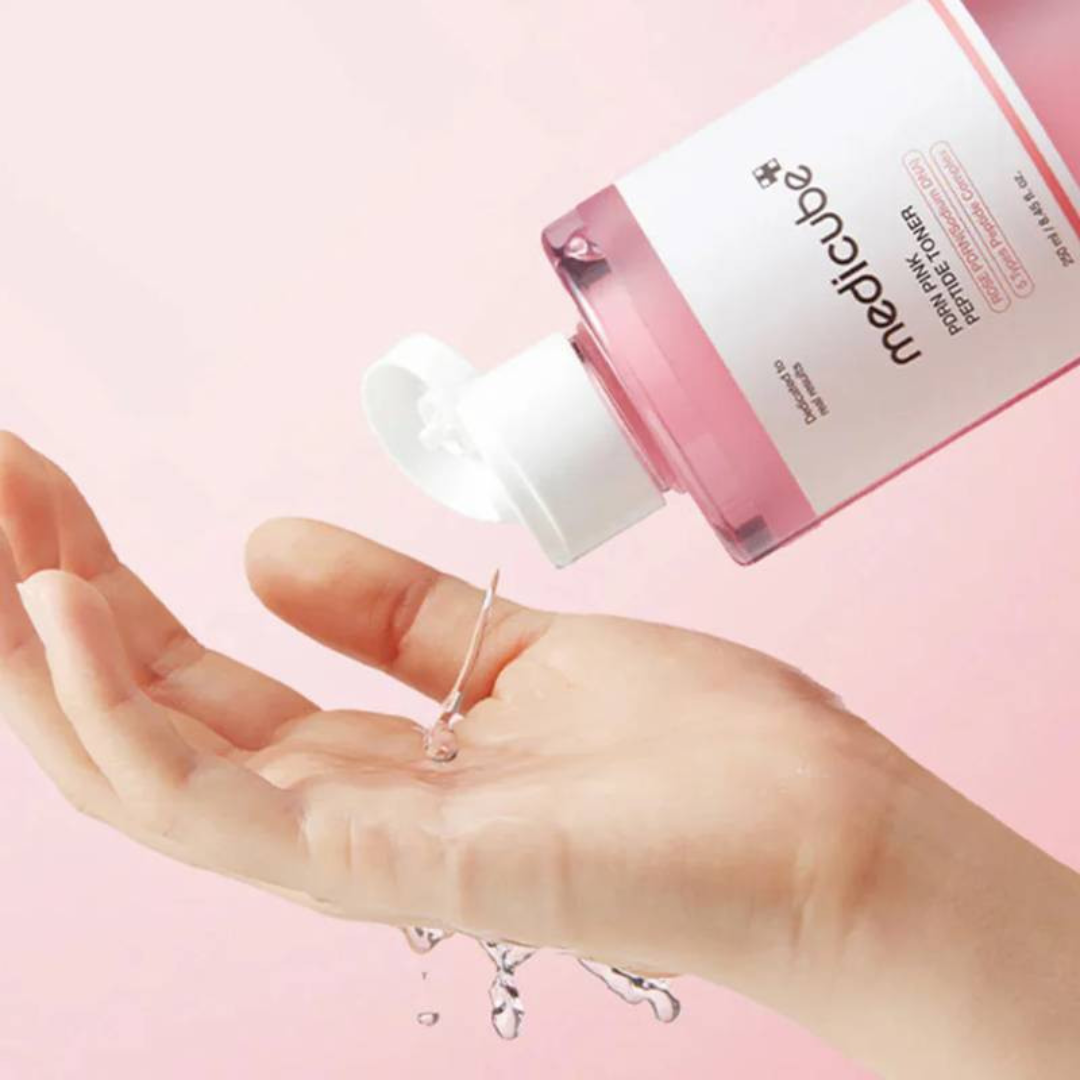 Hand holding a bottle of 'medicube' skincare product with pink liquid on a pink background