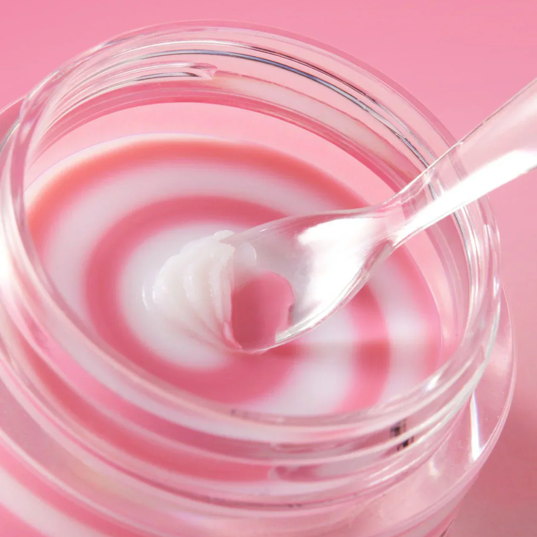 Pink mask in a clear container with a spoon on a pink background