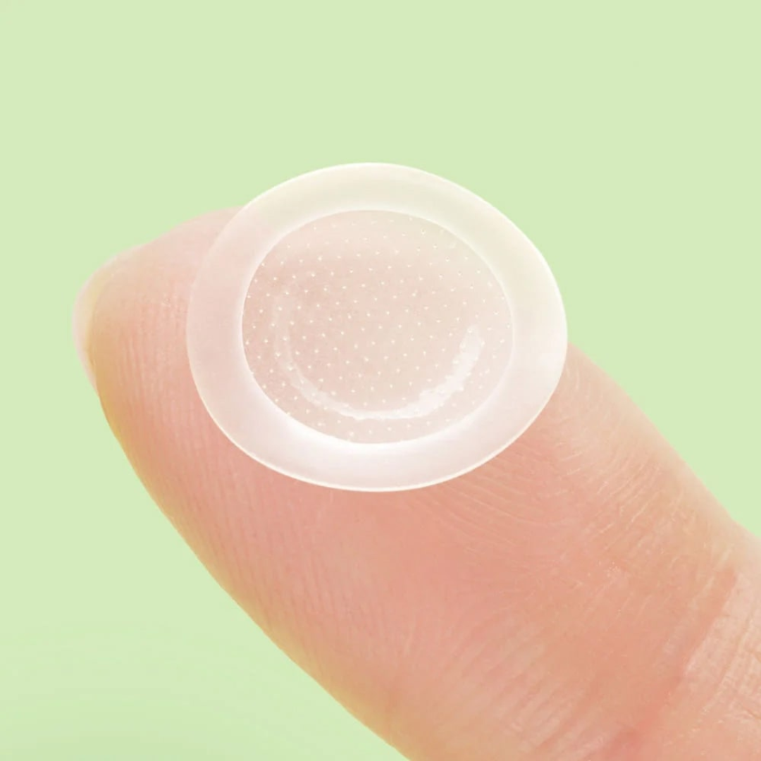 Clear contact lens on a finger against a light green background