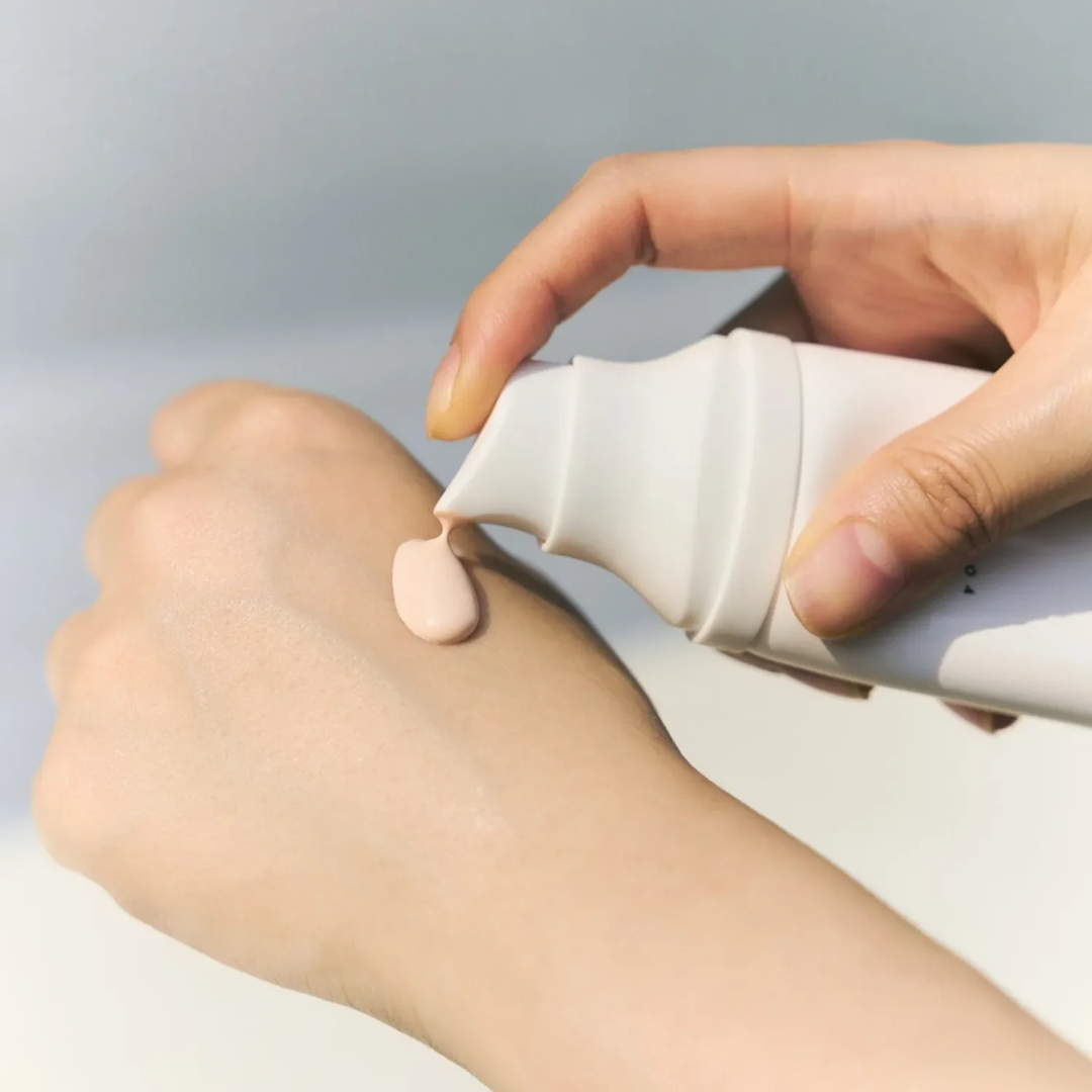 Hand applying a white cream to another hand against a light gray background