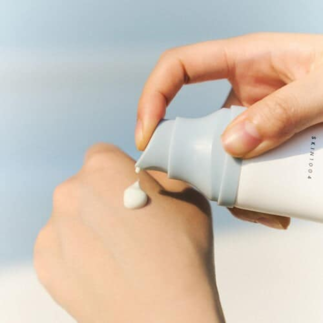 Hand applying cream from a bottle with a light blue background