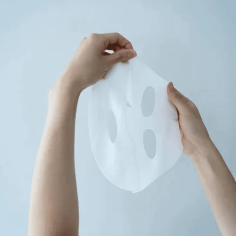 Hands holding a white face mask against a light blue background