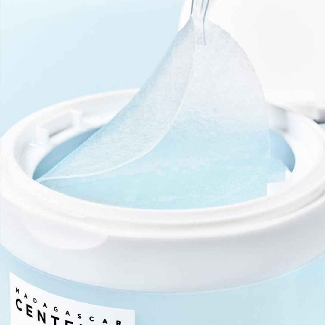 Close-up of a container with a blue liquid being poured into it, featuring the brand 'Madagascar Centella'.