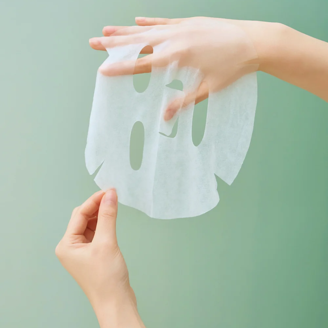 Hands holding a sheet mask against a light green background