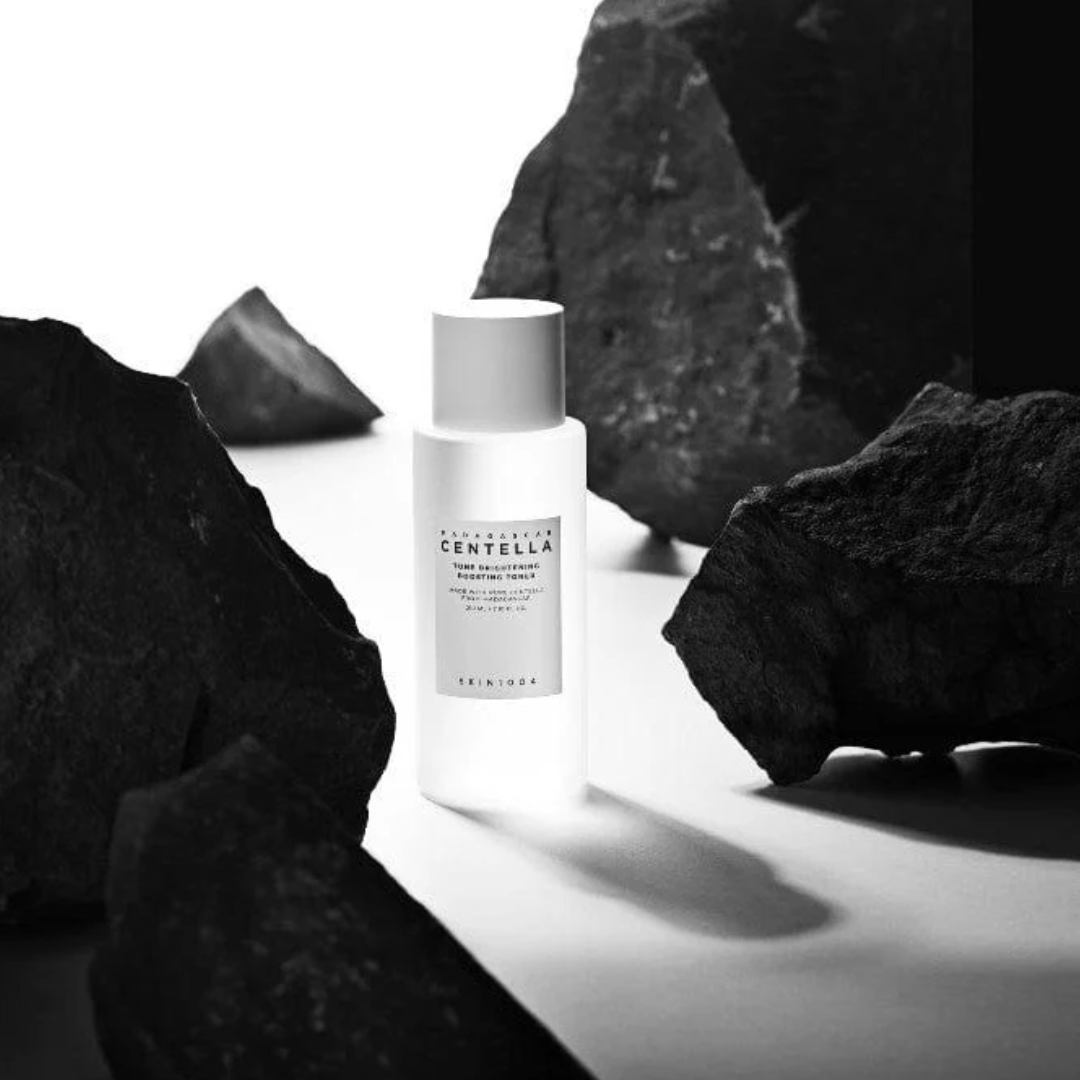 White bottle with label on a white surface surrounded by dark rocks