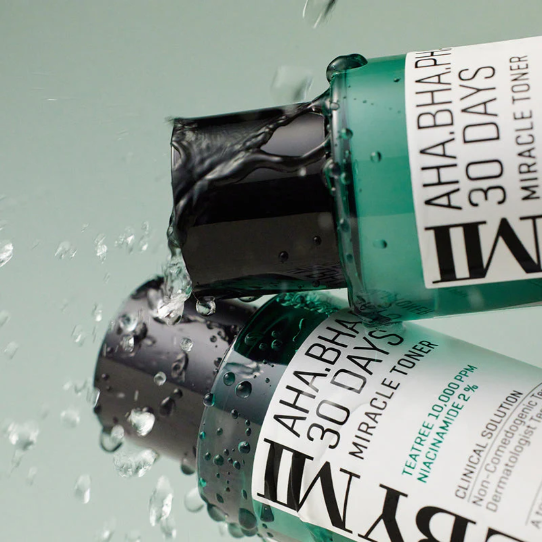 Two bottles of AHA, BHA, 30 Days Miracle Toner by RMK on a light gray background with water droplets.