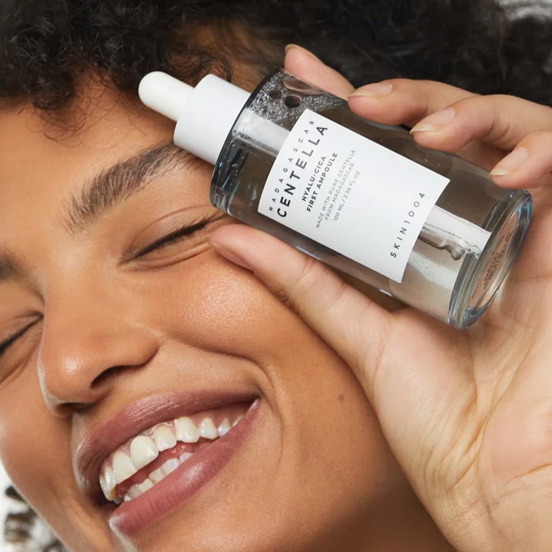 SKIN1004 Madagascan Centella Hyaluronic Acid First Ampoule bottle in a womans' hand by her face with her smiling